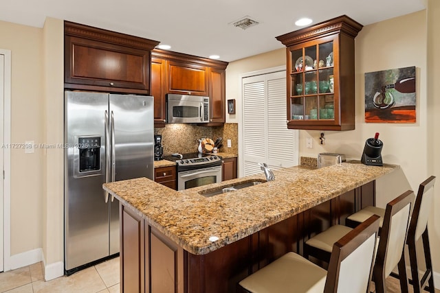 kitchen with kitchen peninsula, sink, appliances with stainless steel finishes, light tile patterned floors, and light stone counters