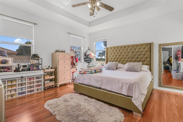 bedroom with a raised ceiling, hardwood / wood-style floors, and ceiling fan