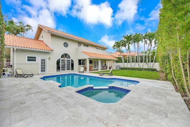 back of house with french doors, a balcony, a lawn, a swimming pool with hot tub, and a patio