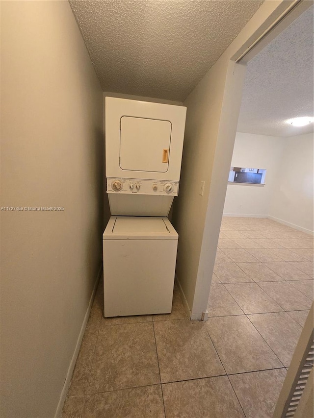 laundry room with stacked washer / drying machine, light tile patterned floors, and a textured ceiling