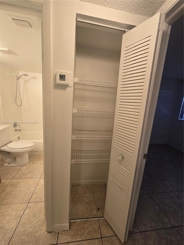 interior space with washtub / shower combination, tile patterned floors, and toilet