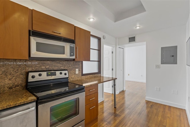 kitchen with dark stone countertops, backsplash, stainless steel appliances, dark hardwood / wood-style floors, and electric panel