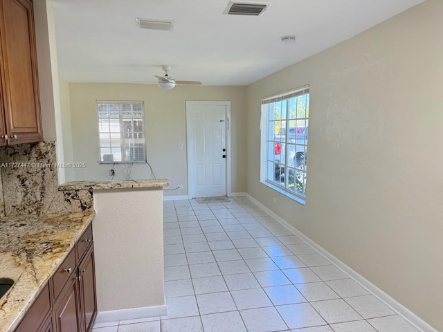 kitchen with light tile patterned flooring, ceiling fan, backsplash, and light stone counters