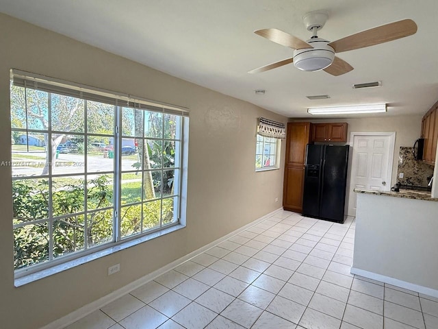 kitchen with black fridge, a healthy amount of sunlight, light tile patterned flooring, and light stone counters