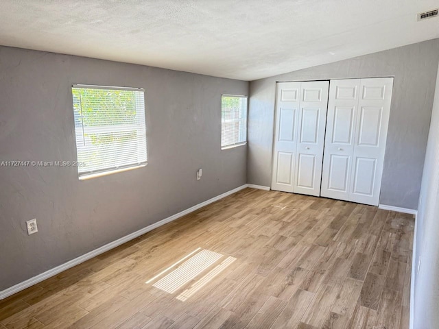 unfurnished bedroom with lofted ceiling, light hardwood / wood-style flooring, a closet, and a textured ceiling