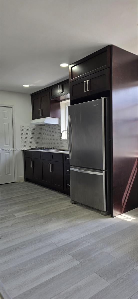 kitchen with light wood-style floors, backsplash, freestanding refrigerator, and under cabinet range hood