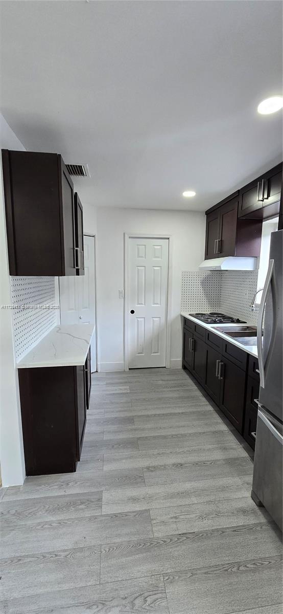 kitchen with visible vents, backsplash, freestanding refrigerator, dark brown cabinetry, and light wood-type flooring