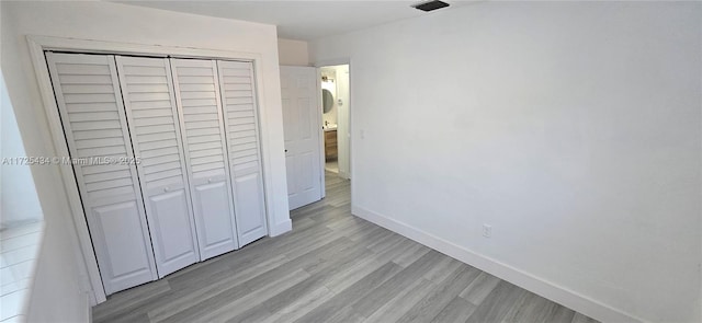 unfurnished bedroom with light wood-style flooring, visible vents, baseboards, and a closet