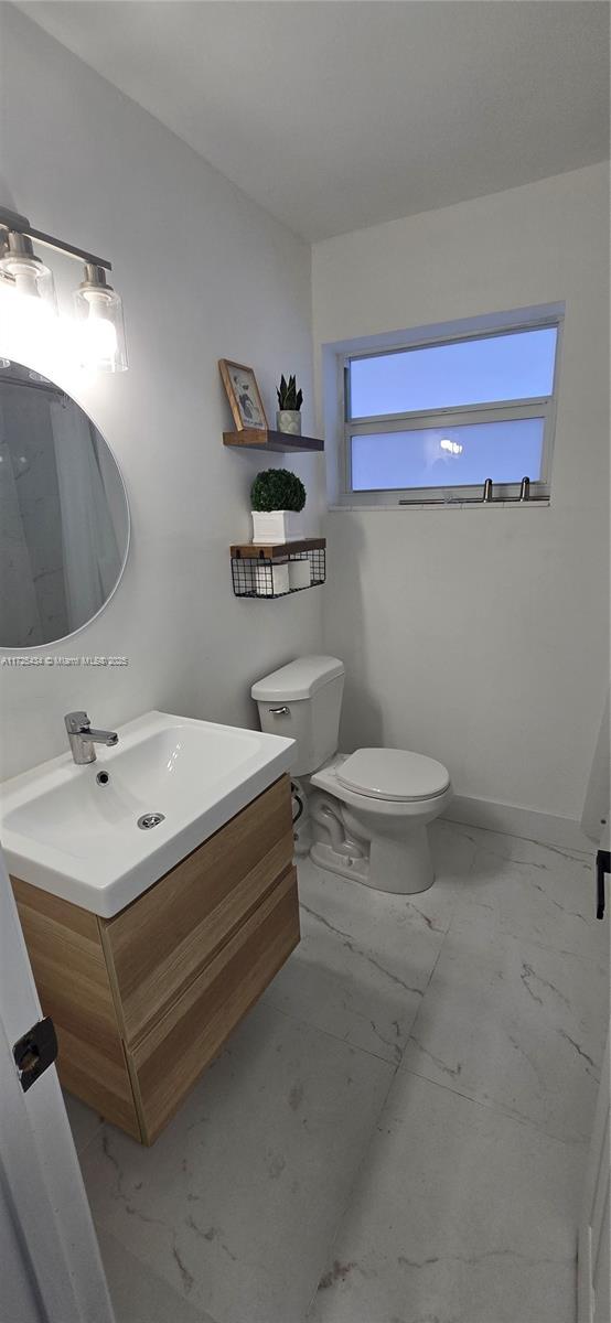 bathroom featuring toilet, marble finish floor, baseboards, and vanity