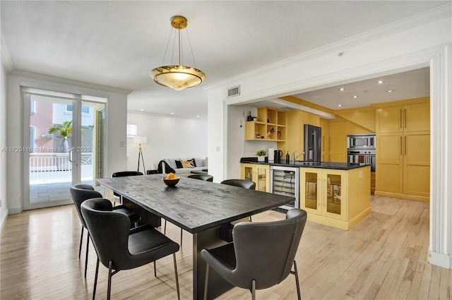 dining space with light hardwood / wood-style floors, crown molding, and wine cooler