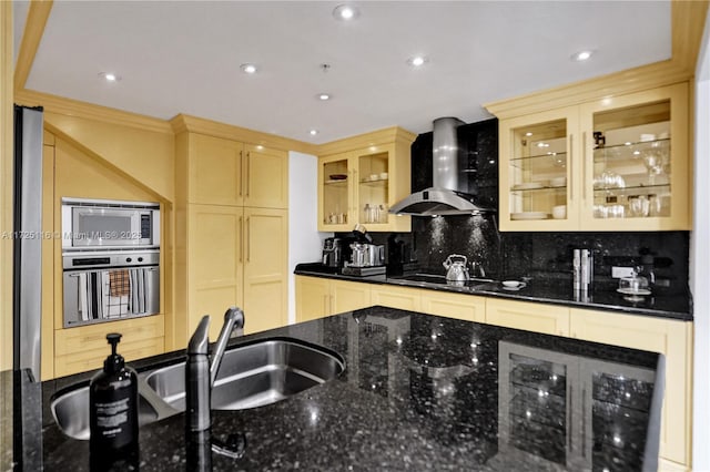 kitchen featuring stainless steel appliances, backsplash, dark stone countertops, wall chimney range hood, and sink