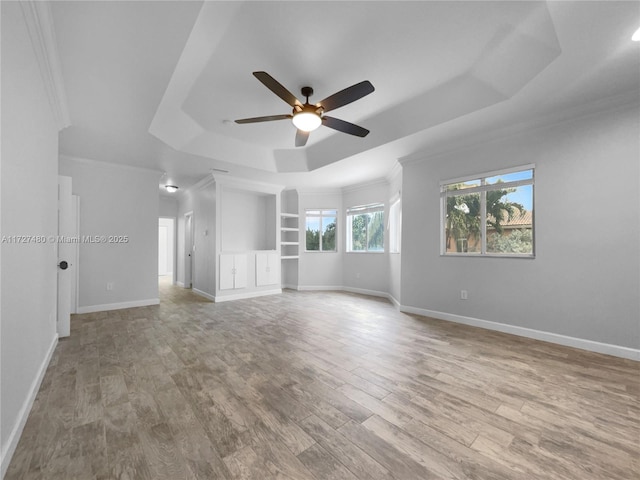 unfurnished room with ceiling fan, crown molding, a tray ceiling, light wood-type flooring, and built in shelves