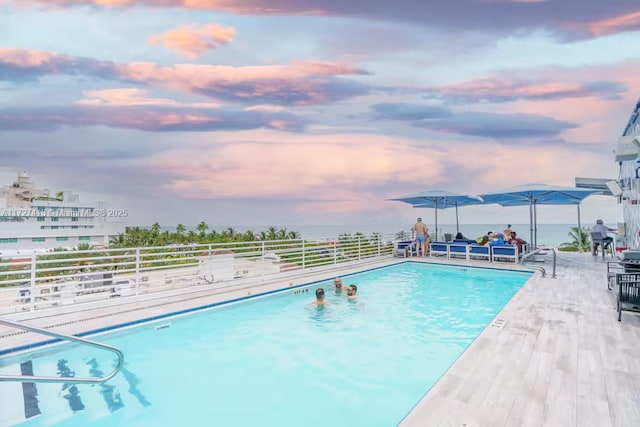 pool at dusk with a patio area and a grill