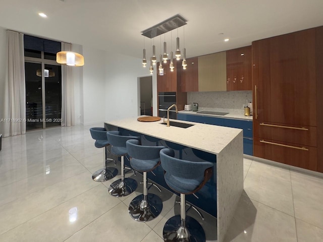 kitchen with an island with sink, decorative backsplash, light tile patterned flooring, pendant lighting, and sink