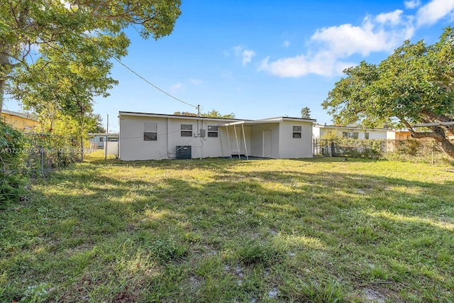 rear view of property with central AC unit and a lawn