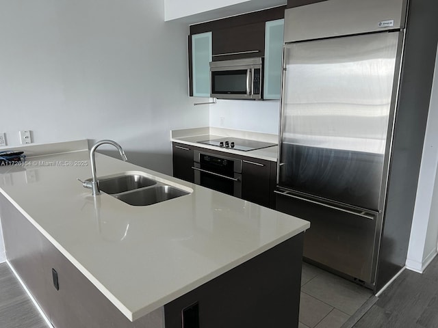 kitchen featuring stainless steel appliances, light countertops, a sink, and dark cabinetry