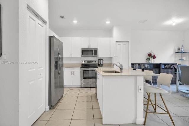 kitchen with a breakfast bar, sink, a kitchen island with sink, stainless steel appliances, and white cabinets