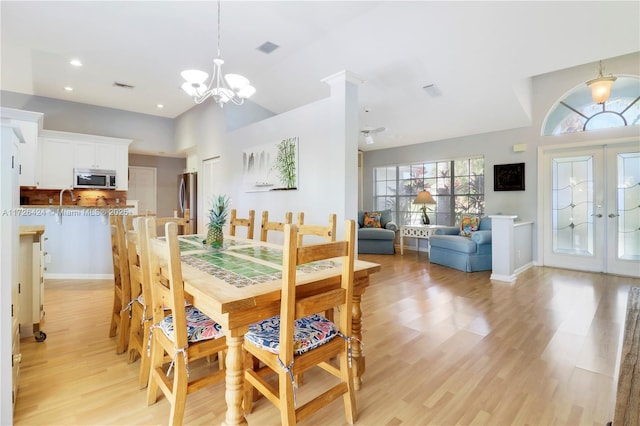 dining area with light hardwood / wood-style floors, french doors, and an inviting chandelier