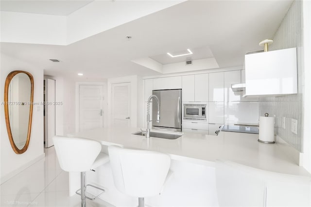 kitchen with white cabinets, a kitchen bar, built in appliances, sink, and kitchen peninsula