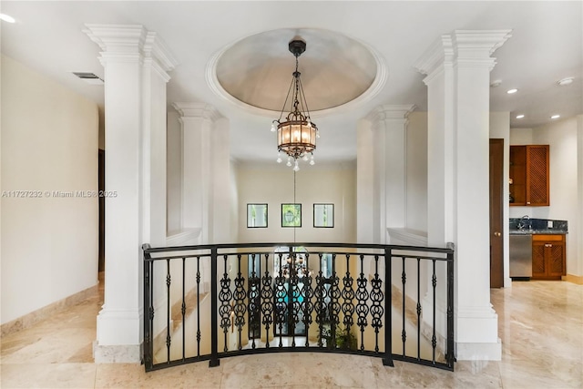 corridor featuring ornate columns, sink, ornamental molding, a raised ceiling, and an inviting chandelier