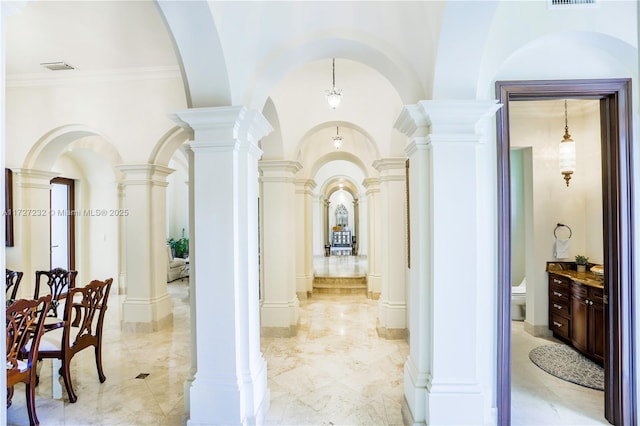 hall featuring vaulted ceiling, ornamental molding, and decorative columns