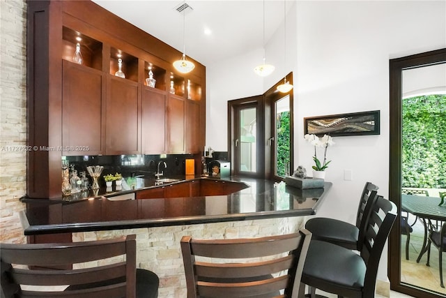 kitchen featuring pendant lighting, a breakfast bar area, dark countertops, visible vents, and a peninsula