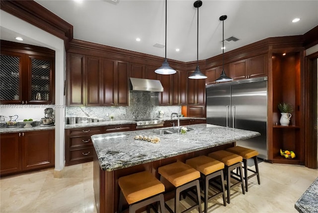 kitchen featuring pendant lighting, exhaust hood, stainless steel built in fridge, and a center island with sink