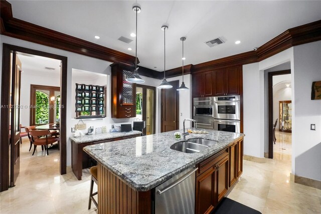 kitchen with stainless steel appliances, a kitchen island with sink, hanging light fixtures, light stone countertops, and sink