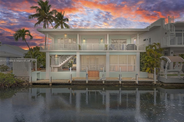 back house at dusk with a water view and a balcony