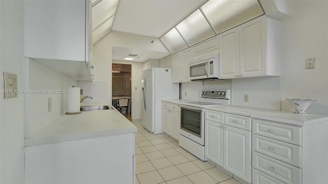 kitchen with lofted ceiling, sink, white appliances, light tile patterned floors, and white cabinetry