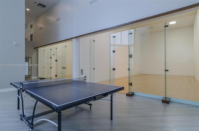 recreation room with visible vents, a towering ceiling, and baseboards