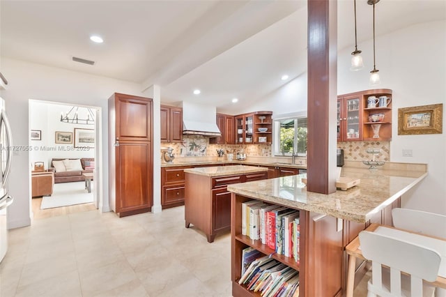 kitchen with hanging light fixtures, light stone countertops, custom range hood, and kitchen peninsula