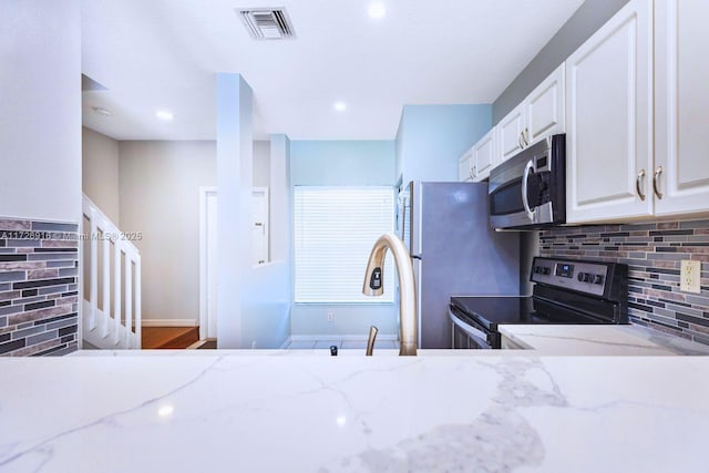 kitchen with white cabinetry, wood-type flooring, decorative backsplash, stainless steel appliances, and light stone countertops