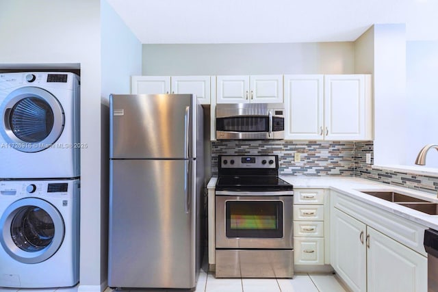 kitchen featuring backsplash, appliances with stainless steel finishes, white cabinetry, a sink, and stacked washing maching and dryer