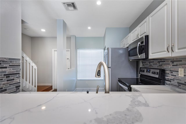 kitchen with white cabinets, stainless steel appliances, visible vents, and light stone countertops