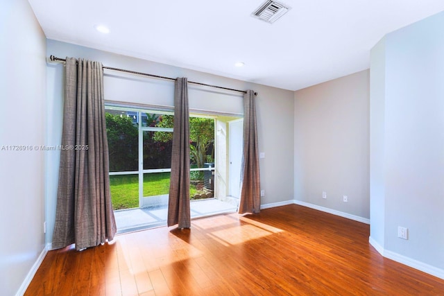 empty room with wood finished floors, visible vents, and baseboards