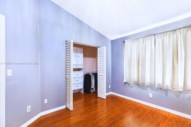 unfurnished bedroom featuring lofted ceiling, dark wood-type flooring, a closet, and baseboards