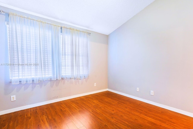 empty room with lofted ceiling, wood finished floors, and baseboards