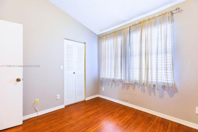 spare room featuring lofted ceiling, wood finished floors, and baseboards