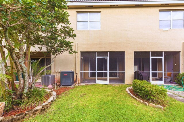 rear view of house featuring a lawn, central AC unit, and stucco siding