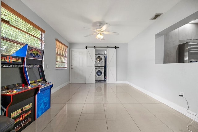 rec room featuring ceiling fan, a barn door, stacked washer and clothes dryer, and light tile patterned floors