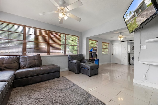 tiled living room with ceiling fan, stacked washer / dryer, and a barn door