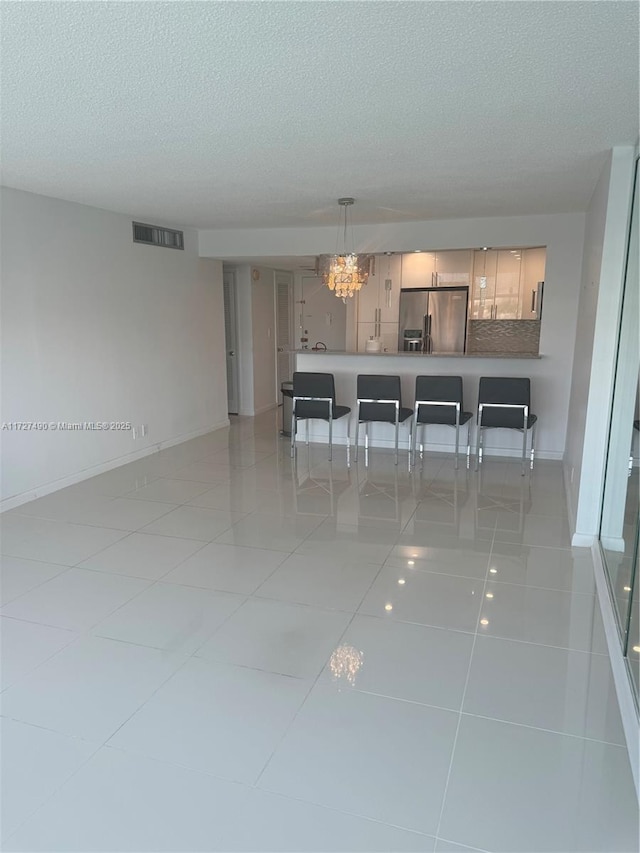 unfurnished dining area with a textured ceiling, light tile patterned floors, and a chandelier