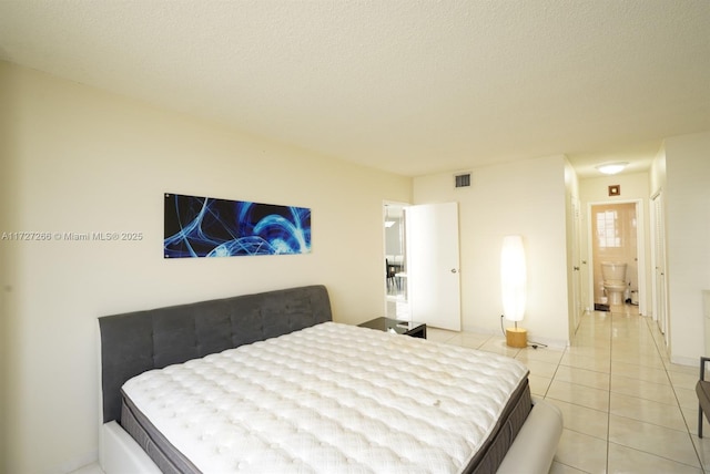 bedroom featuring a textured ceiling, ensuite bathroom, and light tile patterned flooring