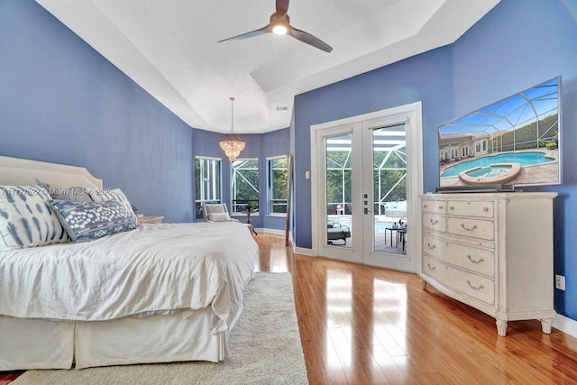 bedroom featuring french doors, access to exterior, ceiling fan with notable chandelier, and a tray ceiling