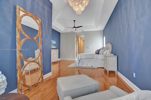 bedroom with a raised ceiling, ceiling fan with notable chandelier, and hardwood / wood-style floors