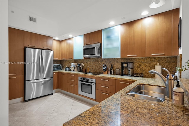 kitchen with appliances with stainless steel finishes, decorative backsplash, light tile patterned flooring, light stone countertops, and sink