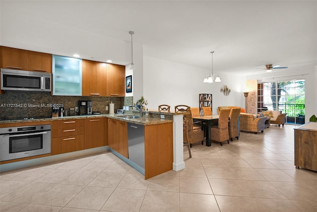 kitchen featuring kitchen peninsula, hanging light fixtures, appliances with stainless steel finishes, light stone countertops, and ceiling fan with notable chandelier