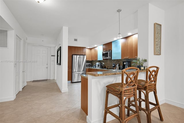 kitchen with pendant lighting, a breakfast bar, kitchen peninsula, decorative backsplash, and appliances with stainless steel finishes