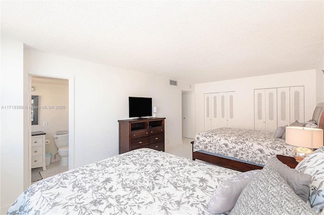 bedroom featuring a textured ceiling, multiple closets, and ensuite bathroom